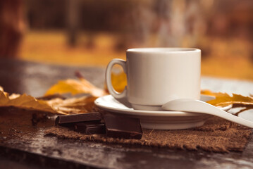 A cup of coffee on a wooden table in the park among autumn foliage. Cup of tea on an autumn day