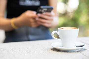 Cup of latte on the wooden table in the cafe shop. A beautiful shadow appeared. Woman's hand holding smart phone in cafe shop