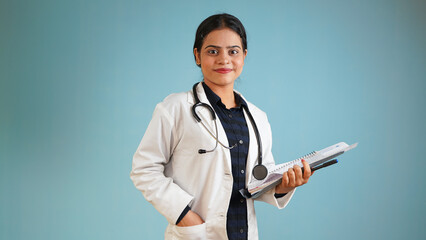 Portrait of a young female doctor wearing apron and stethoscope, Cheerful Asian Indian woman doctor isolated over blue studio background