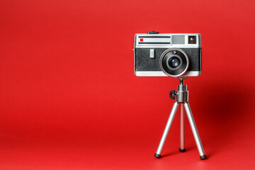 Vintage 60s metal photo camera on aluminium mini tripodon a red background.