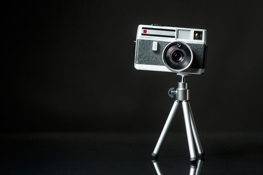 Vintage 60s metal photo camera on aluminium mini tripodon a black background.