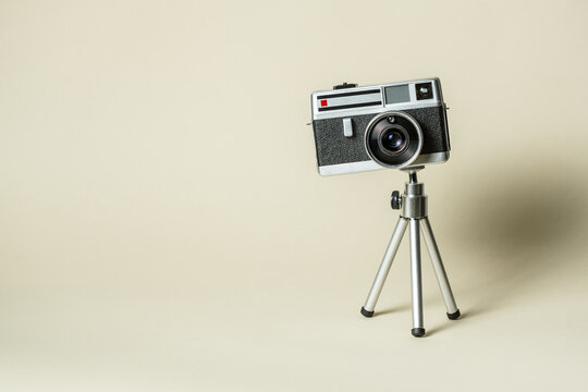 Vintage 60s metal photo camera on aluminium mini tripodon a beige background.