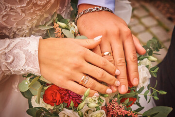 Obraz na płótnie Canvas Groom and bride holding hands with gold wedding rings on wedding bouquet, close-up without faces.