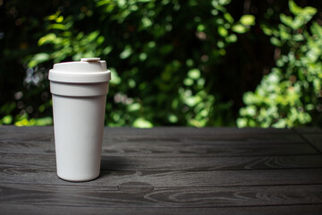 Obraz premium white coffee cup on black wooden table with green leaves background