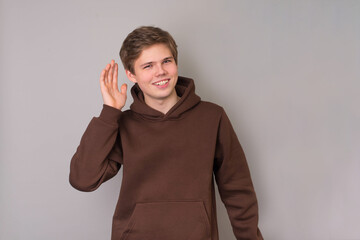 Teenager in hoodie holds his hand to his ear to hear something or show he is listening, paying...