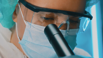 Scientist in goggles and mask using microscope.