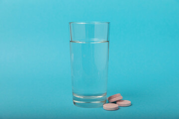 An effervescent vitamin tablet drops and dissolves in a glass of water on a blue background. The concept of health. Medicine concept. Place for text.