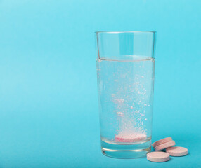 An effervescent vitamin tablet drops and dissolves in a glass of water on a blue background. The concept of health. Medicine concept. Place for text.
