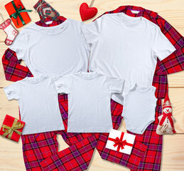 Blank white t-shirts for the whole family on the background of bright pajamas on a wooden background with Christmas presents