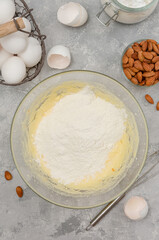 Recipe step by step. The process of making Italian cantucini cookies. Whipped eggs with sugar, butter, flour and baking powder in a bowl on a gray concrete background. Top view.