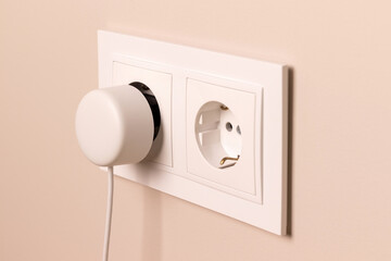 Group of white european electrical outlets with round plug inserted into it on modern beige wall