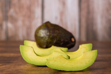 Avocado chunks on a rustic wooden table, with an avocado in the background out of focus, foreground.