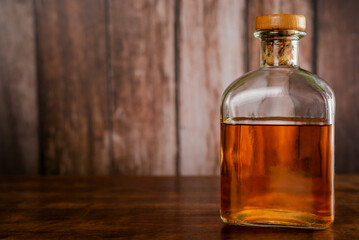 Bottle with whiskey on a wooden table and a rustic background, copy space.