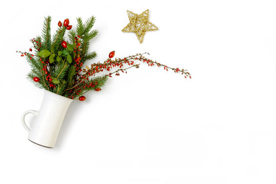 White ceramic cup with bouquet of spruce, barberry twigs and wild rose fruits on white background with rustic golden star, top view, copy space, still life
