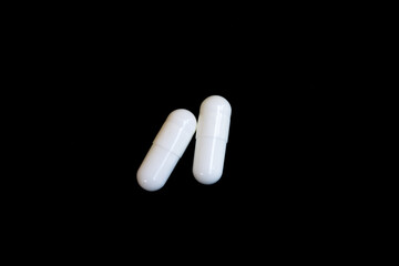 Two white capsule pills on black background isolated object.