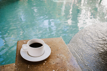Morning coffee in a saucer in front of a bright blue pool background