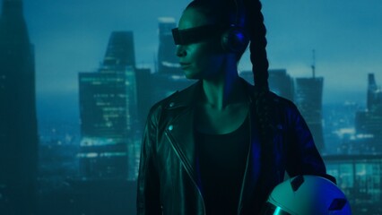 Portrait of cyberpunk girl with a smartphone in a glasses and headphones. Beautiful young woman on the background of city scyscrapers. © Acronym