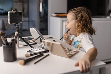 a cute little cheerful girl 4-5 years old blogger, makes a make-up telling the subscribers of the channel on the phone camera, the concept of blogging