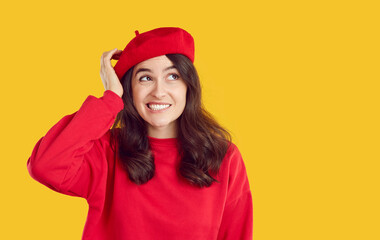 Confused smiling brunette emotional woman in red beret and sweatshirt looking aside on copy space yellow background. She scratches her head in thought. Doubted, puzzled, thinking girl making decision.