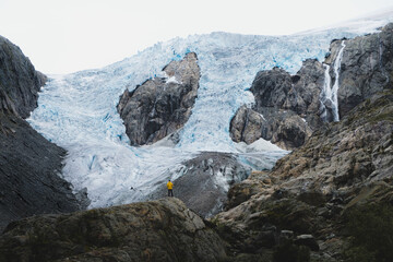 Hiker in yellow jacket in front of majestic glacier in Norway, Buerbreen glacier