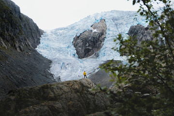 Hiker in yellow jacket in front of majestic glacier in Norway, Buerbreen glacier