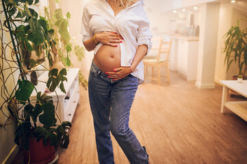 Cropped shot of pregnant woman standing at home holding hands on her belly