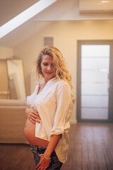 Portrait of pregnant woman standing at home holding hands on her belly