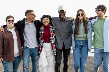 Best multiethnic young friends walking and talking carefree arm on shoulders - group of multiracial people embracing together seaside