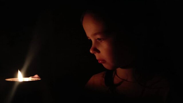 A child plays by candlelight. Lack of electricity in Ukraine. War in Ukraine. Blackout in Ukraine. Russian aggression in Ukraine. Ukrainian child plays by candlelight. Children against war