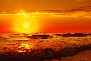 Fototapeta na wymiar The sun is sinking into the sea. The sun's rays pass through the waves, smoothly rolling onto the shore. A bright orange sunset over the sea is magnificent. the concept of a romantic summer vacation.