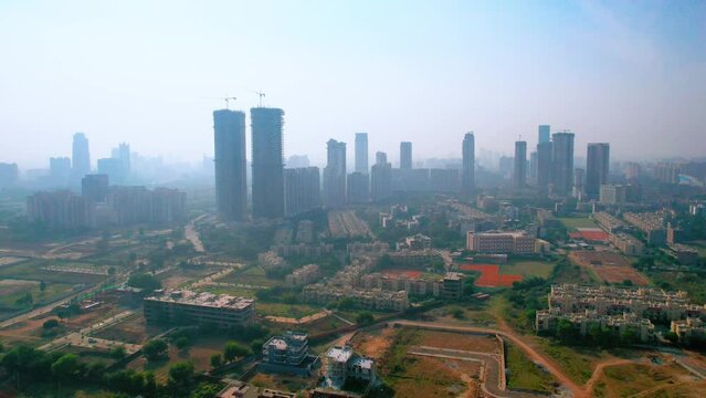 aerial orbit drone shot of fog smog hidden twin skyscrapers with smaller buildings in the distance empty feilds and houses showing the cityscape of Gurgaon delhi outskirts under development