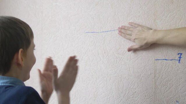 the concept of children grow up, mother measures the growth of a caucasian boy and draws a mark on the wall, the boy is half a year old, the boy's 8th birthday