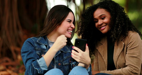 Diverse girls looking at cellphone screen. Woman calling friend to check out of content online