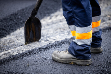 Road construction or reparation and worker with shovel spreading new layer of asphalt. - obrazy, fototapety, plakaty