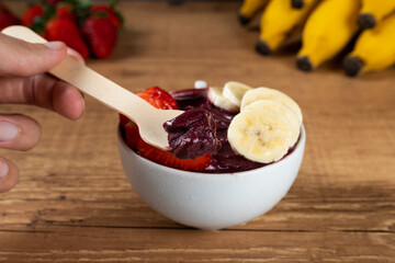 Hand holding an Brazilian Açai Bowl with Banana and Strawberry on a wooden background