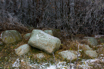 Winter landscape with old snow-covered stones at the edge of the forest against the background of frost-covered branches.