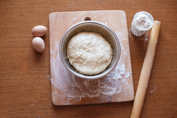 Utensils and ingredients for baking, top view, raw yeast dough in a bowl and ingredients - eggs, flour, rolling pin on the kitchen table. Baking concept, copy space. Culinary background.