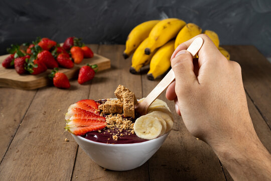 Spoon and a White Bowl of Brazilian Frozen A&ccedil;ai Berry With Pa&ccedil;oca, Strawberry and Banana. on a wooden desk