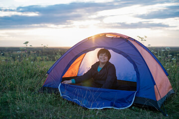 Hacker teen boy  resting in a touristtentristtent campsite enjoying view of beautiful summer nature at sunset.