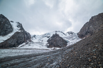 Dramatic landscape with two glacier icefalls on large snow mountain range with sharp rocks under gray cloudy sky. Long glacier with icefall in high altitude. Gloomy scenery in mountains in overcast.