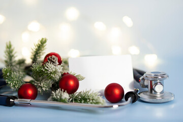 Medical christmas composition with stethoscope and white mockup for text close-up and fir branches in snow on blue background.