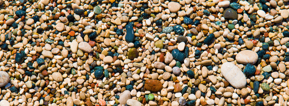 Multi-colored pebbles on the beach of mediterranean sea. Wide photo. Natural background.