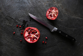 Top flatlay view of a knife and sliced pomegranate showing the seeds and pulp