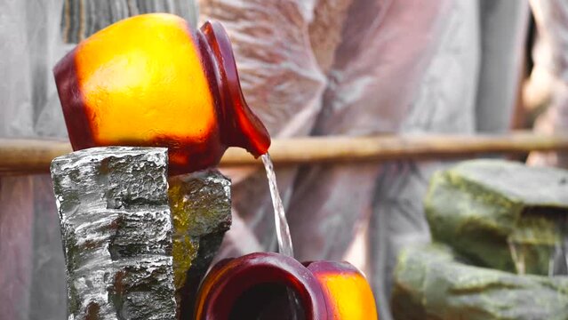 slow motion shot of waterfall fountain with yellow pot pouring water placed in banjara market outdoor place to get handmade, handicraft items for home decoration