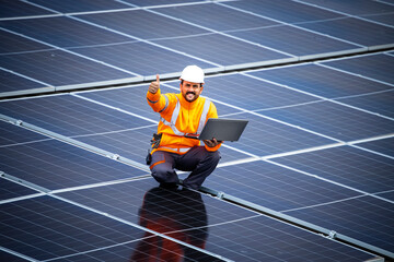 Engineer inspector holding laptop and working in solar panels power plant checking photovoltaic cells and electricity production.