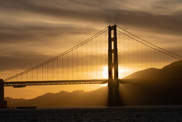 Fototapeta na wymiar Golden gate bridge at sunset with a yellow., gold, brown and black sky and Marin County shown to the right. 