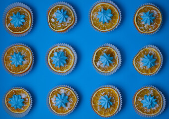bright sweet delicious orange oranges in white muffin tins sprinkled with white powder and decorated with blue mini cakes on a bright blue background. for menu signage labels for cookbook splash scree