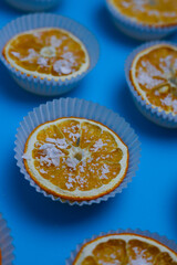 bright sweet tasty orange oranges in white muffin tins sprinkled with white sprinkles on a bright blue background. for menu signage labels for cookbook splash screens