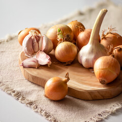 Onions and garlic lie on the table on a wooden board and a canvas napkin.