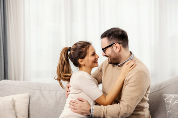 A happy couple is hugging in a living room and looking at each other.